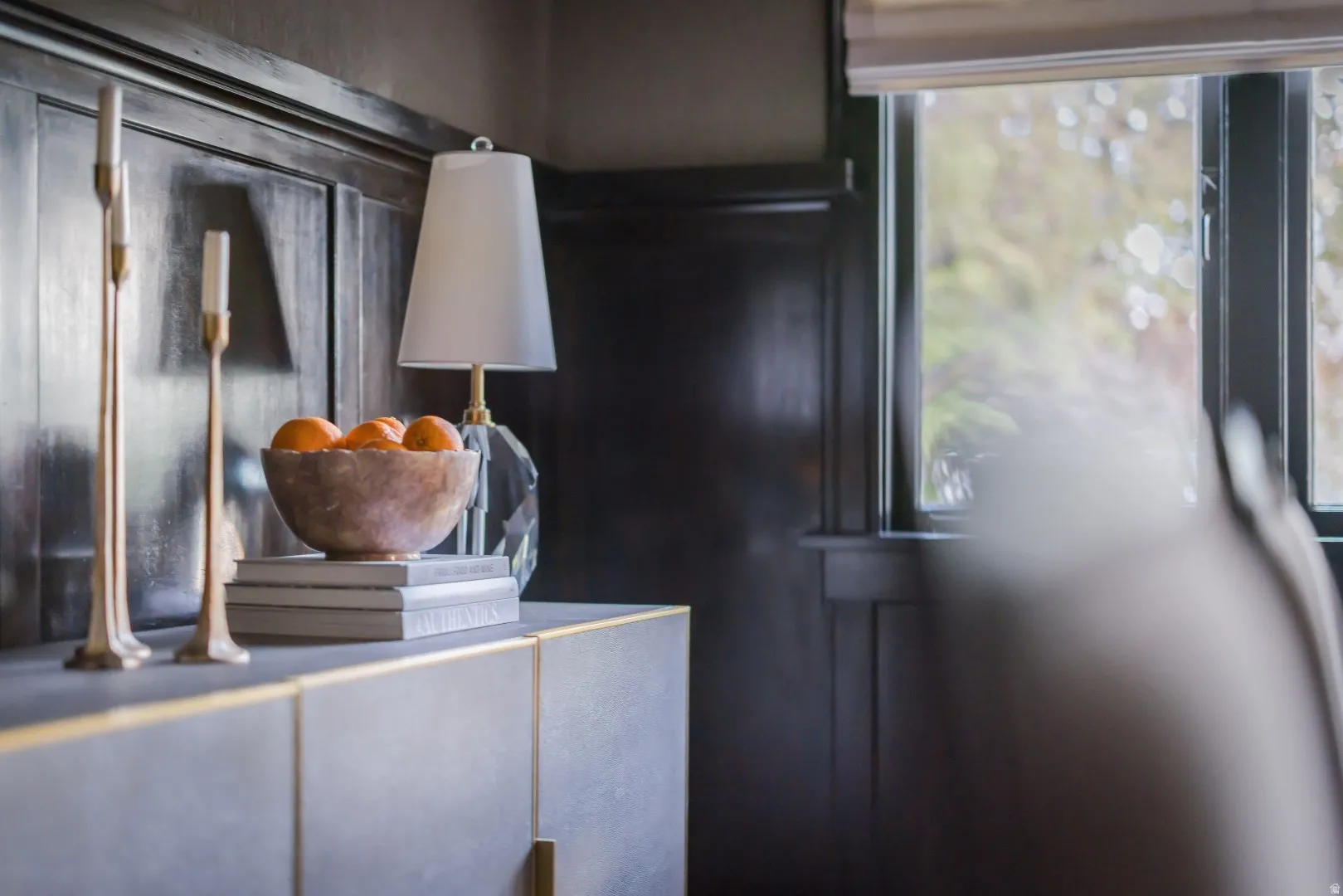 Dark paneled wall featuring a window with a roller shade