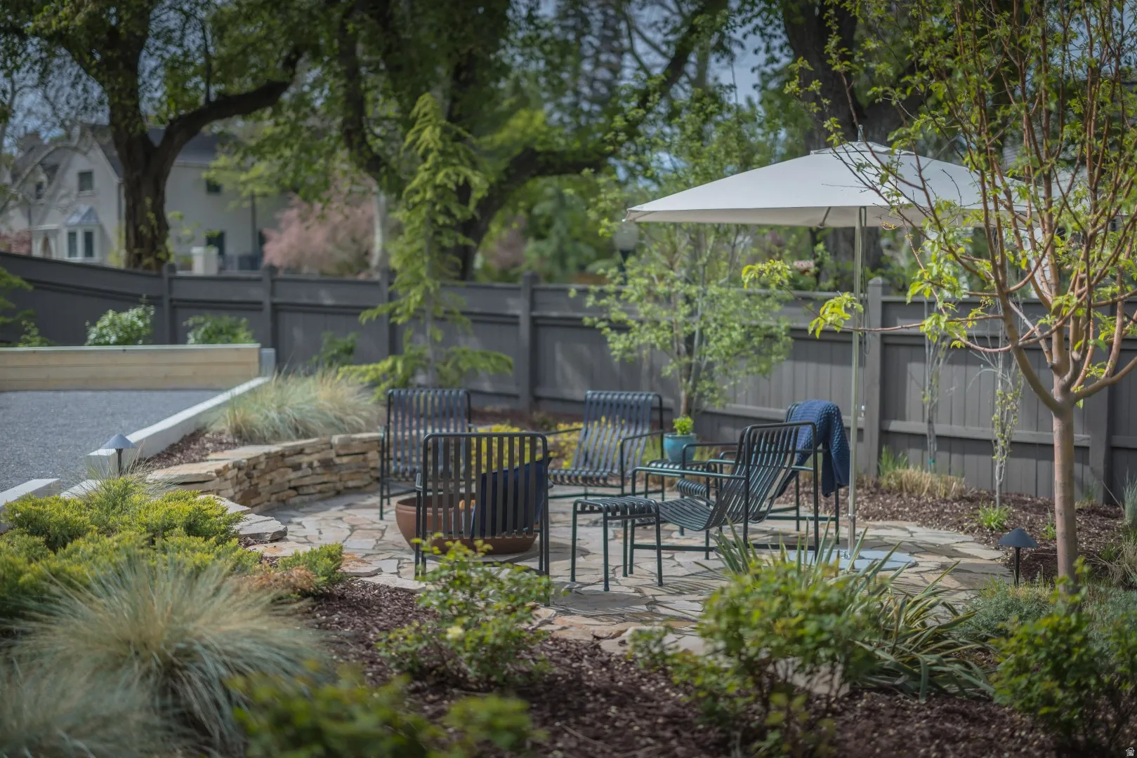 Stone patio with a low stacked stone retaining wall, gravel bocce court with concrete border, and a privacy fence