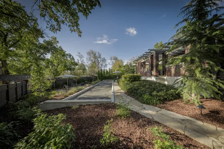 Expansive outdoor space featuring a bocce ball court, flagstone pathway, mature trees, and landscaping