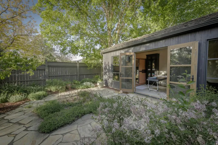 Detached structure with vertical wood siding and double glass-paneled doors, complemented by a flagstone patio and surrounding landscaping