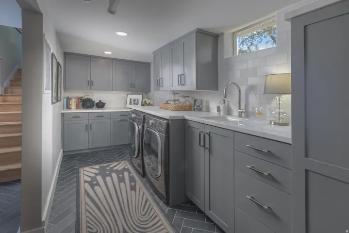 Herringbone pattern tile flooring, extensive gray cabinetry with modern hardware, white countertops, subway tile backsplash, and a built-in sink with a gooseneck faucet