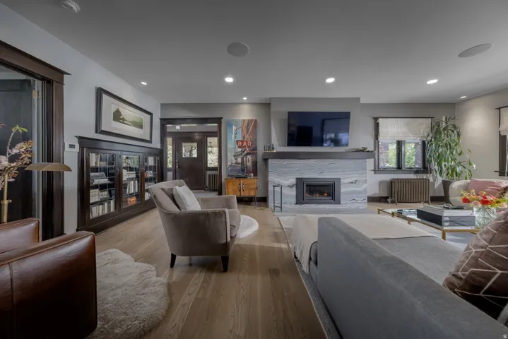 Light wood-finish flooring, built-in fireplace with a stone surround, built-in dark wood cabinetry, recessed lighting, and dark wood trim