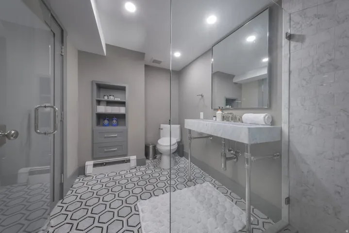 Hexagonal tile flooring, full-height marble shower surround, wall-mounted vanity with integrated sink, rectangular mirror, and recessed lighting