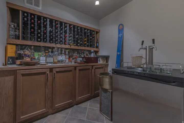 Built-in wine storage, extensive cabinetry with wood-finish doors, countertop space, tiled flooring, and a beverage refrigerator with a double tap