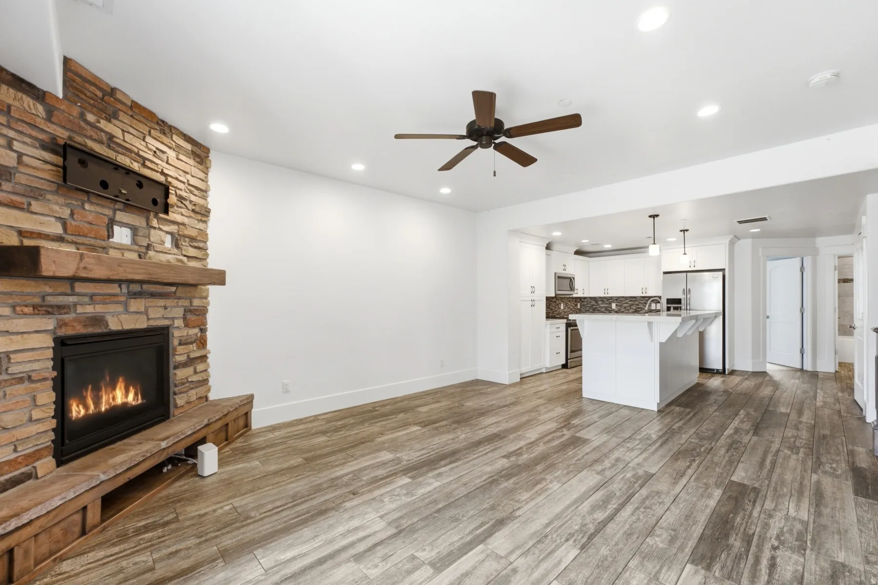 Stone-clad fireplace with wood mantle, wood-finish flooring, recessed lighting, and a ceiling fan