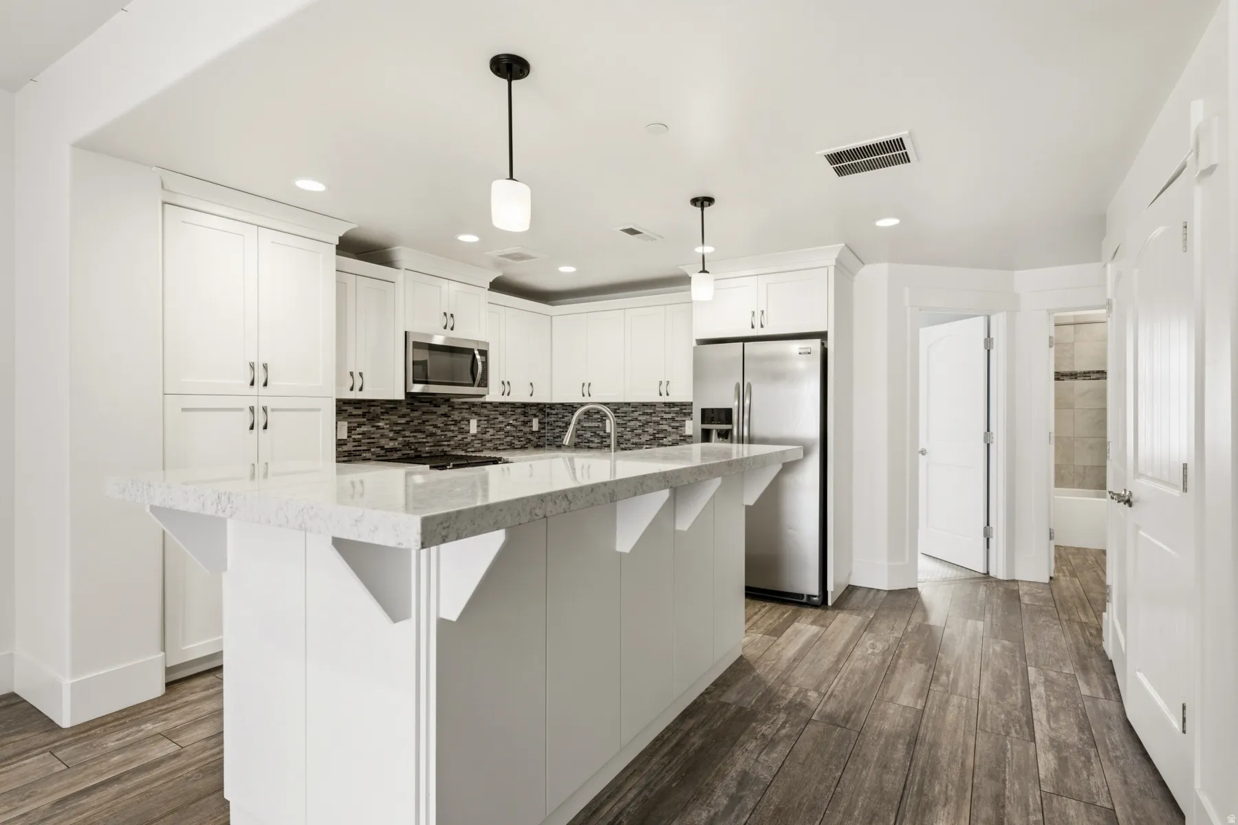 Kitchen featuring a large island with a light-toned countertop, white cabinetry, stainless steel appliances, a mosaic tile backsplash, and wood-finish flooring