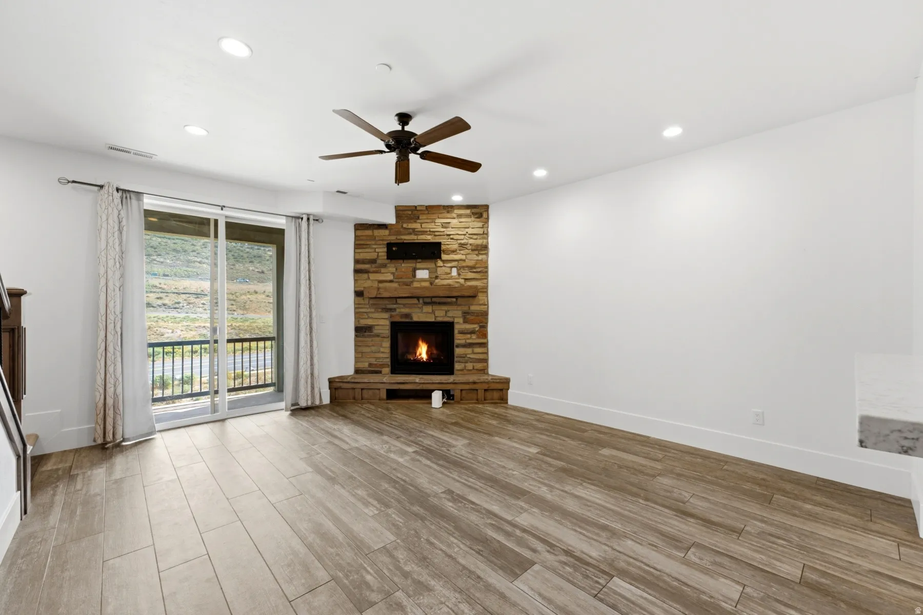 Spacious living area featuring wood-finish flooring, a corner stone-clad fireplace, recessed lighting, and a ceiling fan