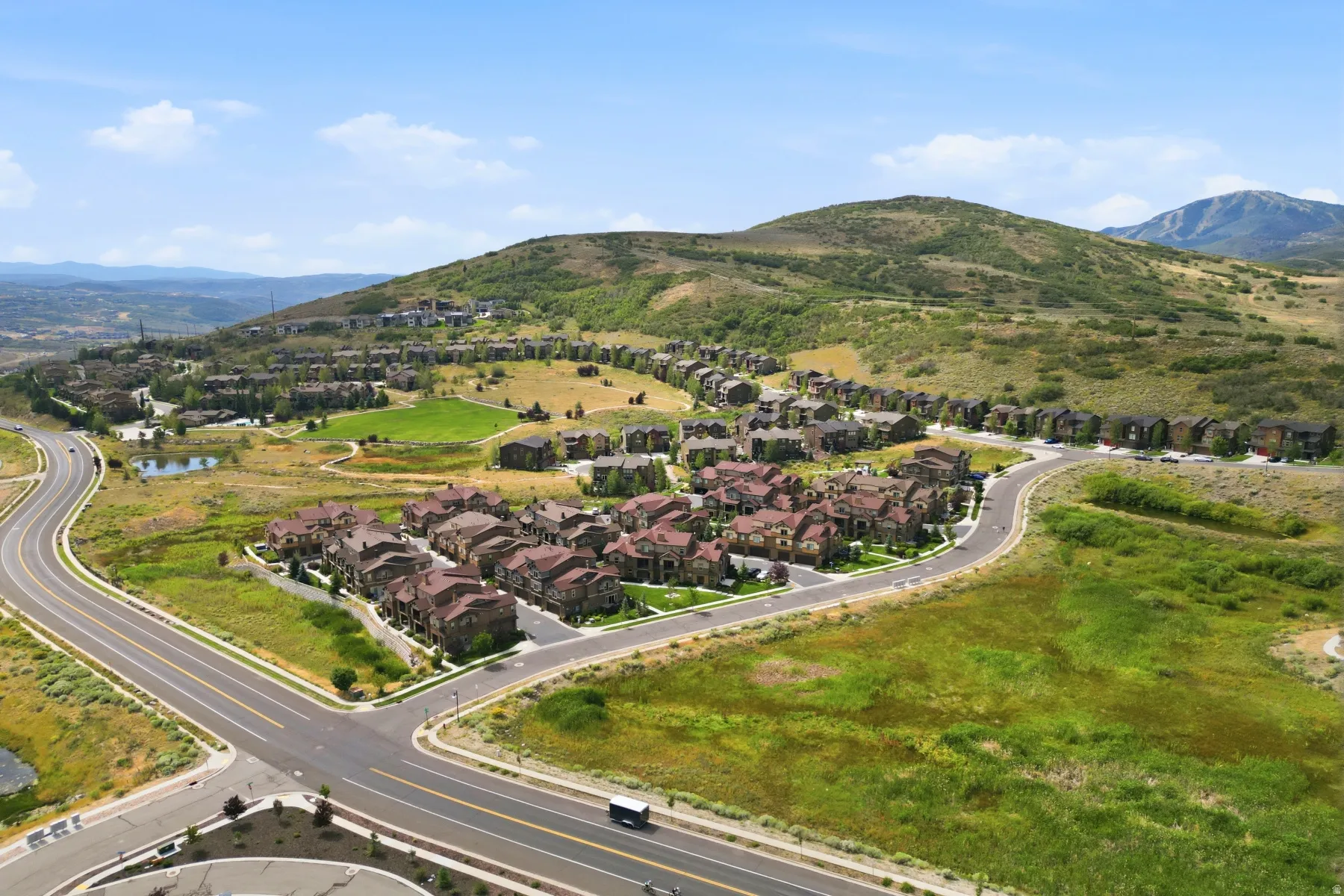 Residential development featuring multiple homes, paved roads, and natural landscaping with undulating terrain