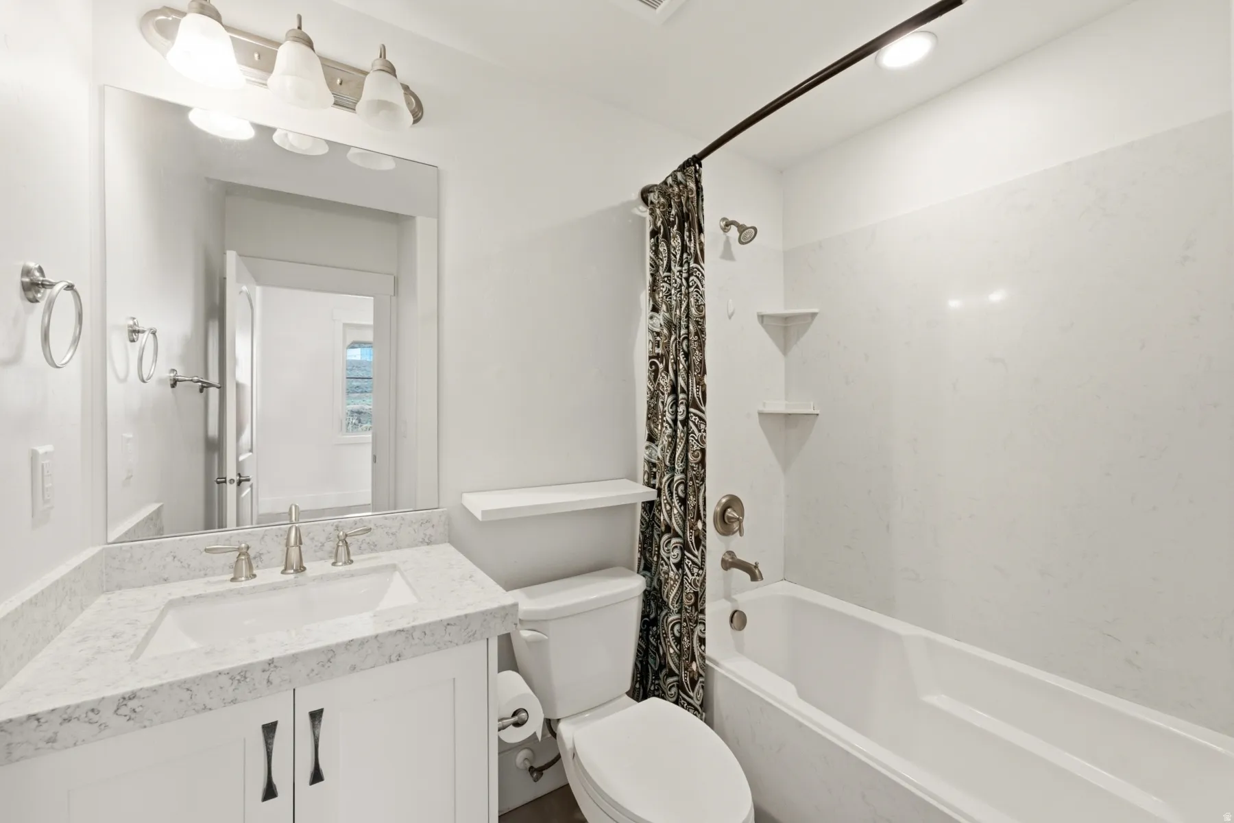 Spa-inspired bathroom featuring a white subway tile surround, marble-topped vanity with dual handles, recessed shelving, polished chrome fixtures, and a soaking tub with a curved shower rod and patterned shower curtain