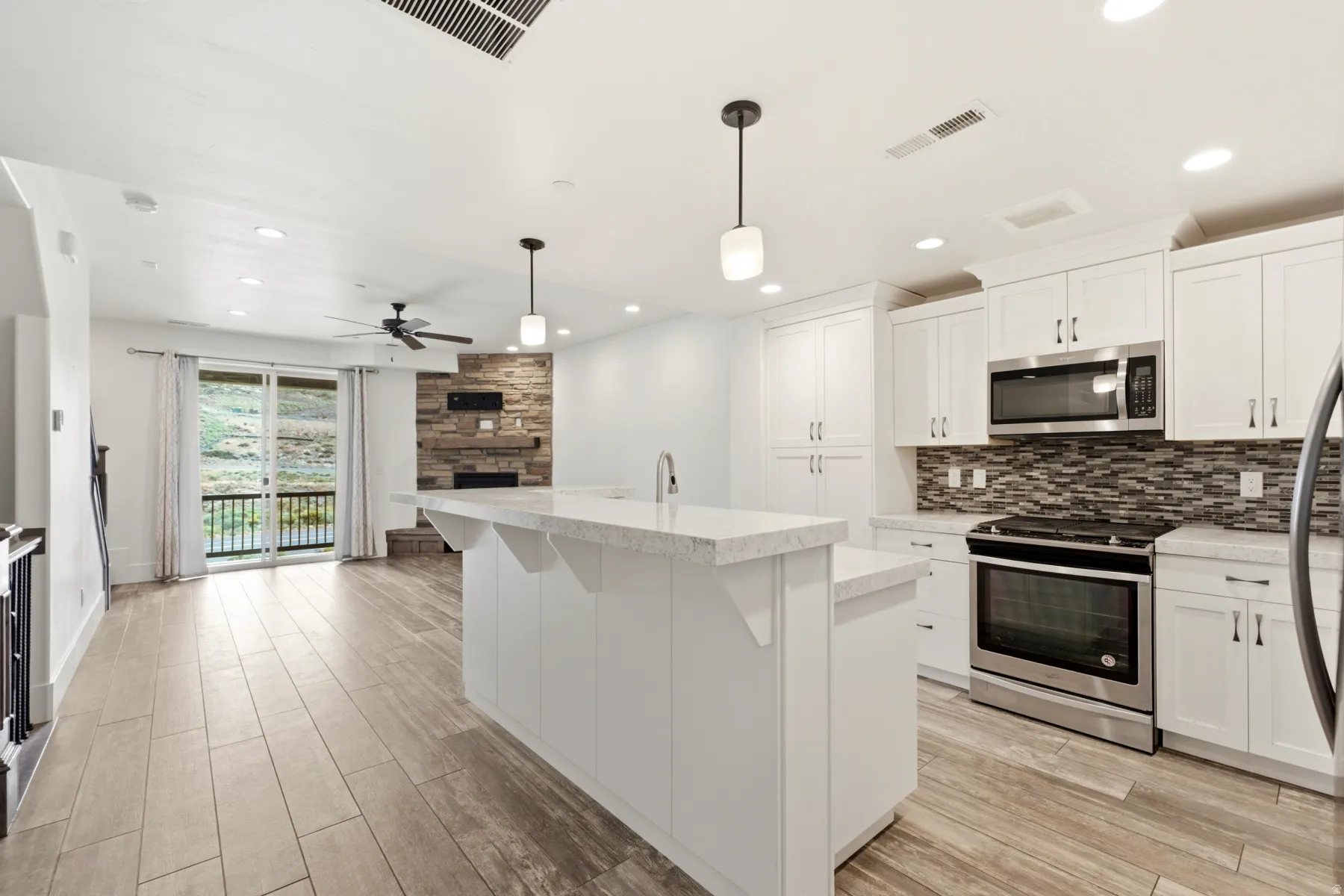 Open-concept kitchen with white cabinetry, stainless steel appliances, and a central island with a waterfall countertop