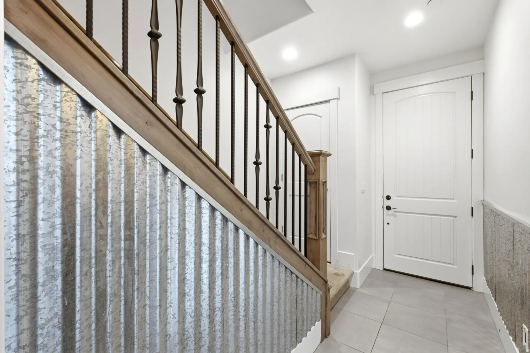 Staircase with wood-finish handrail and wrought iron spindles, complemented by a corrugated metal wall panel