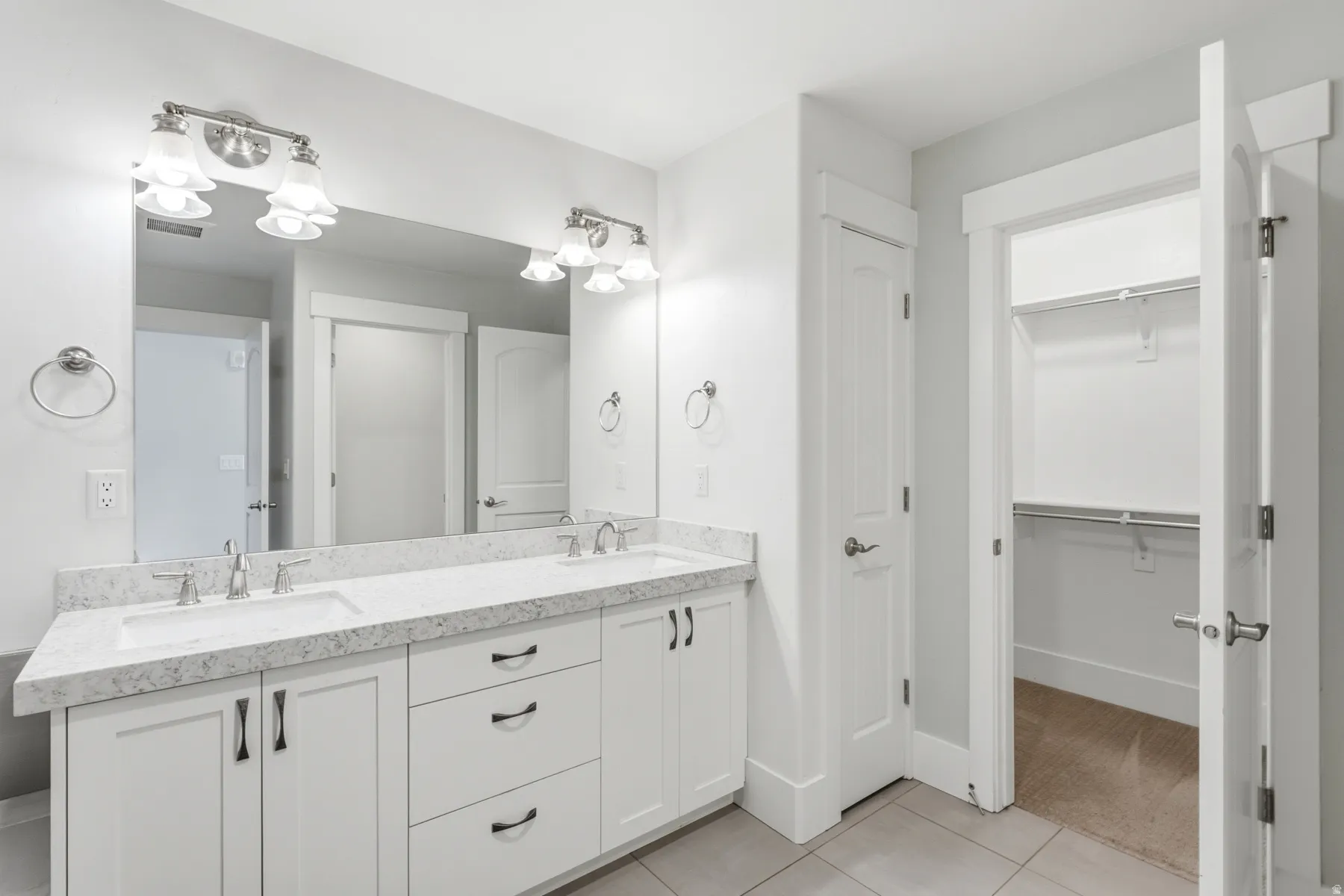 Dual vanity with undermount sinks, stone countertop, white cabinetry with dark hardware, and overhead lighting fixtures