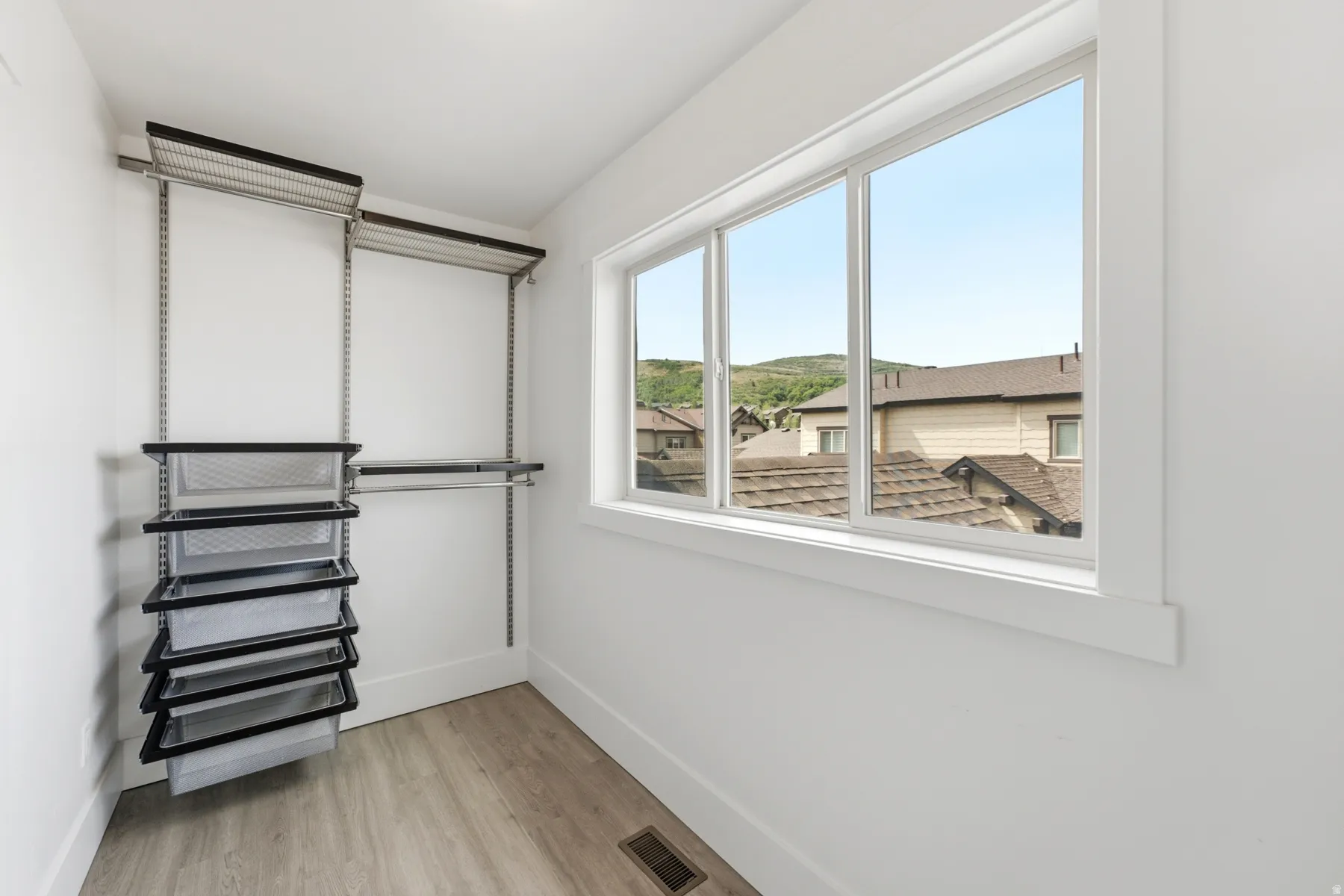 Adjustable closet shelving system, integrated wire drawers, large window, white trim, and wood-finish flooring