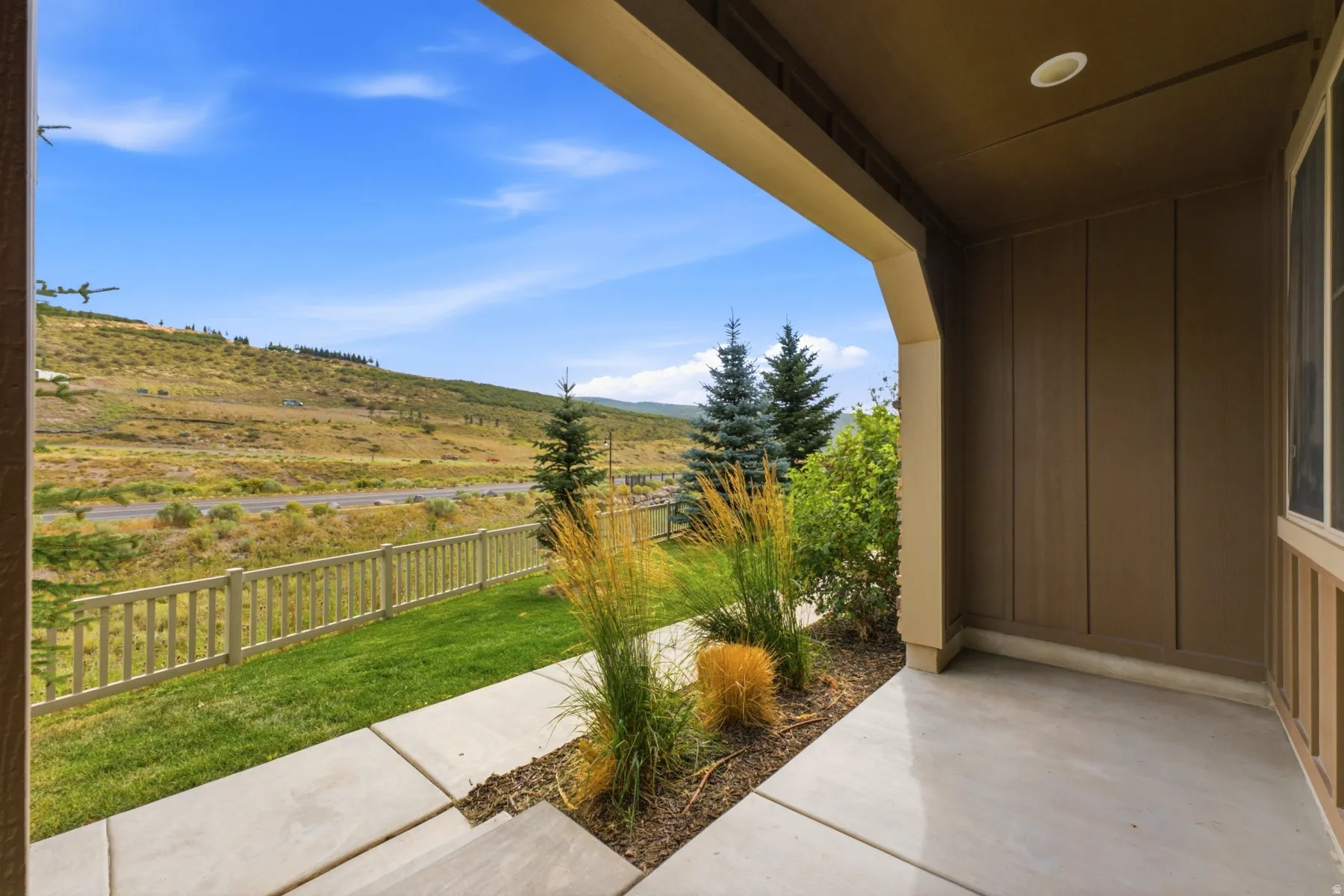 Covered entryway with recessed lighting, concrete pathway, and landscaped planting beds