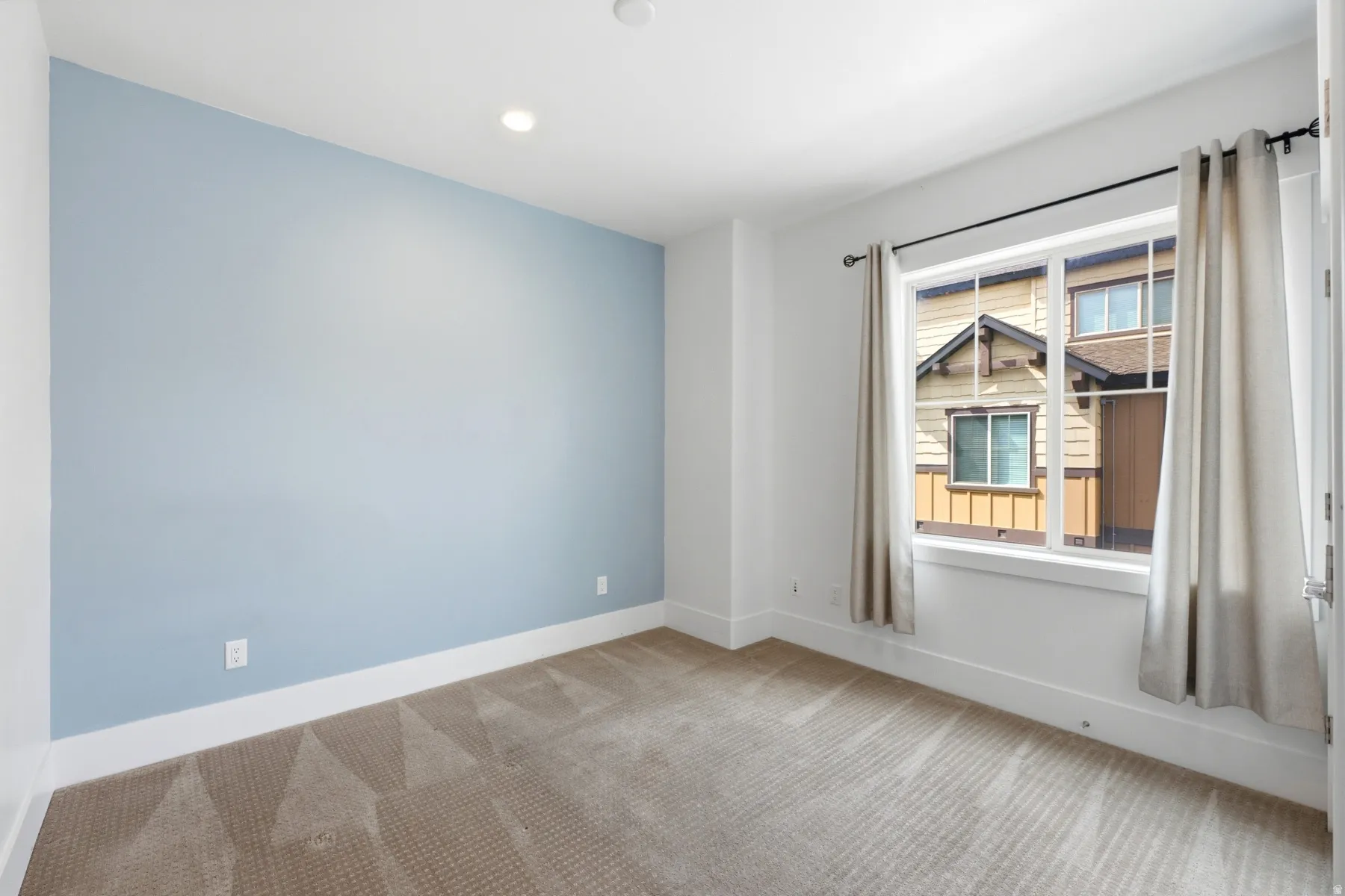 Recessed ceiling lighting, carpeting, a single window with white trim, and a light blue accent wall
