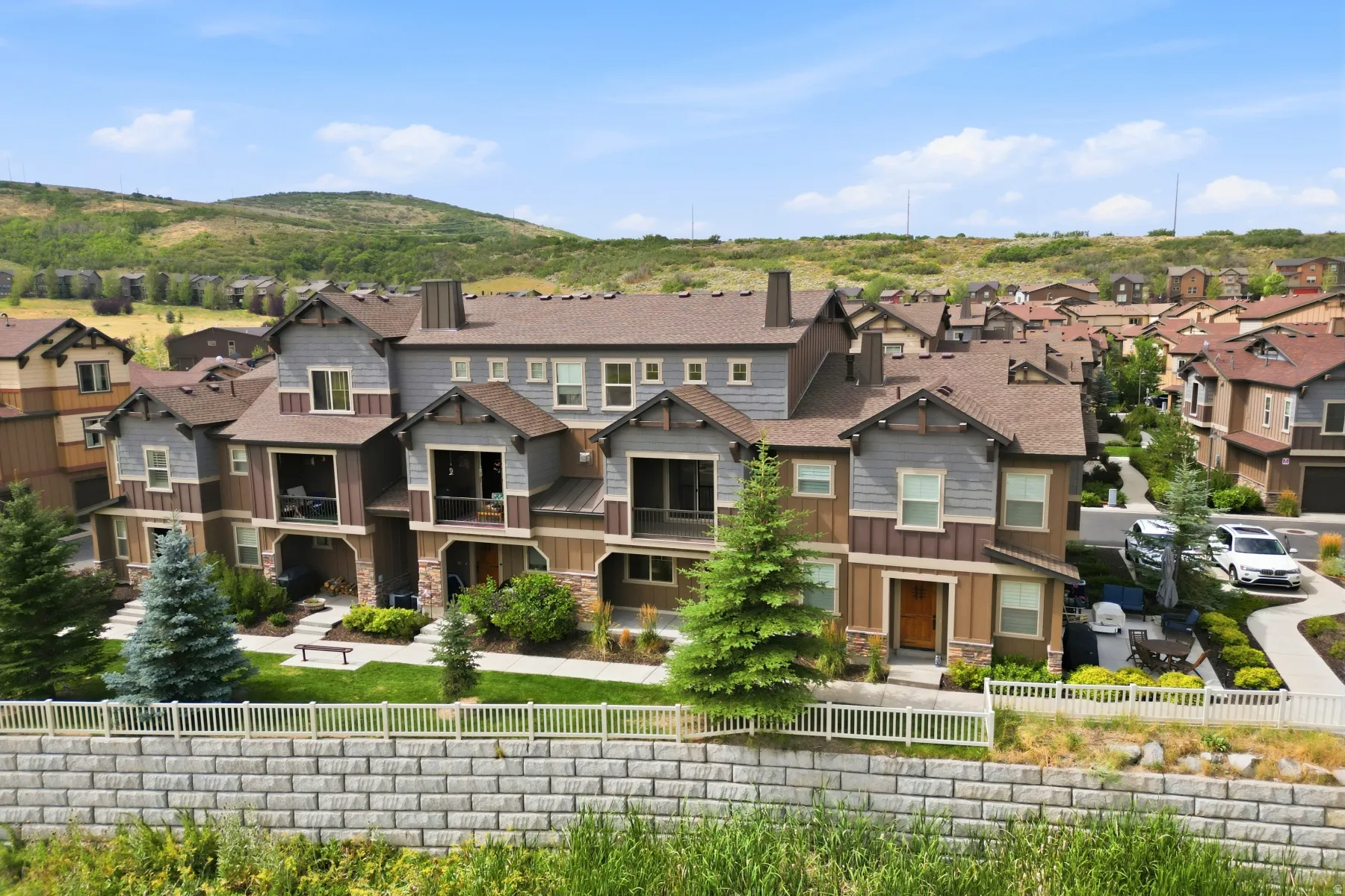 Townhome community featuring multi-level residences with balconies, stone and siding exteriors, and a landscaped common area with a retaining wall