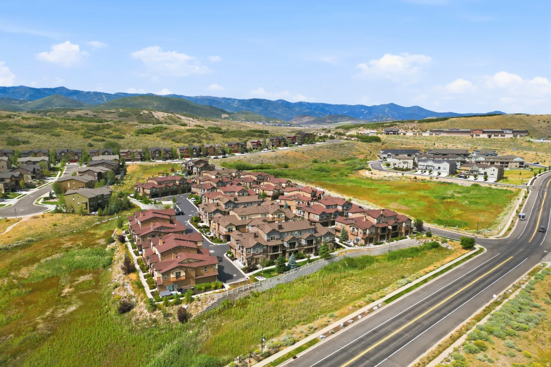 Residential community with varied architectural styles, paved roadways, and surrounding natural landscapes, set against a backdrop of distant mountains