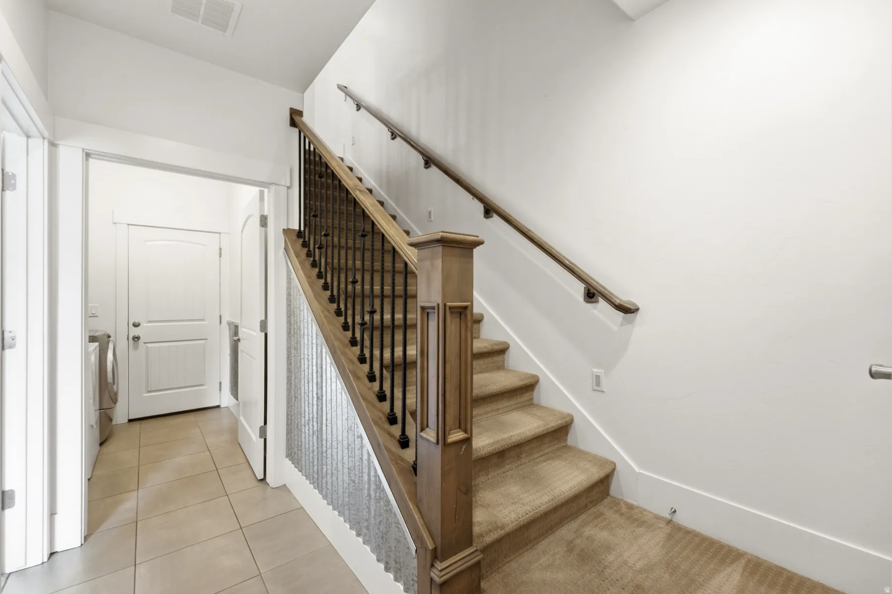 Carpeted staircase with wood-finish handrail and black metal balusters
