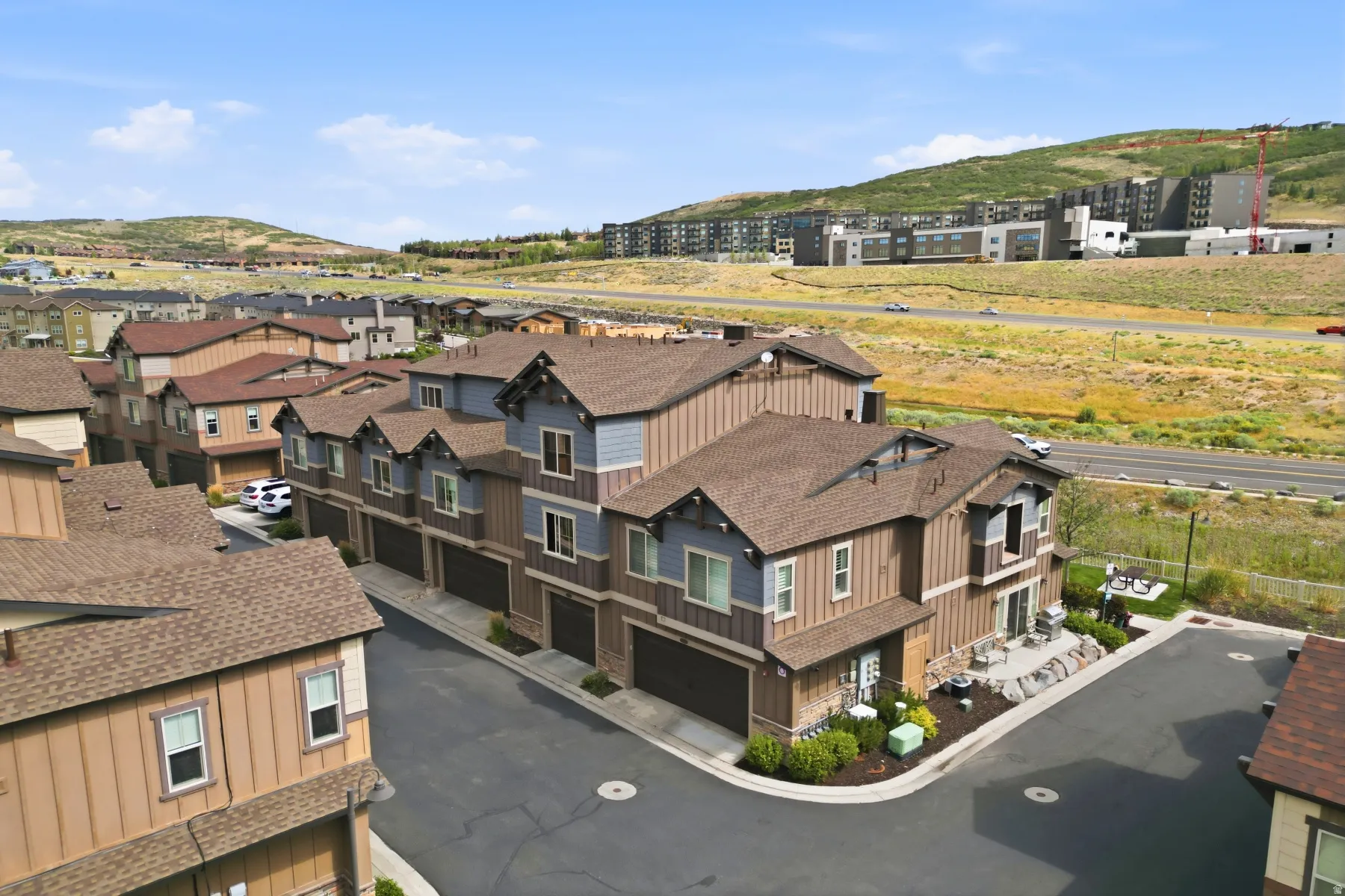 Townhome complex featuring multi-story units with attached garages, individual patios, and a contemporary architectural design with varied siding materials