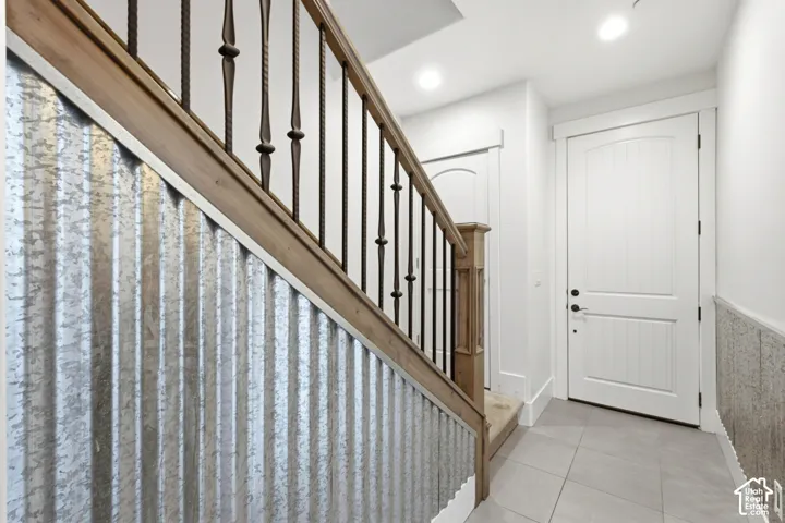 Wrought iron stair balusters with a wood handrail, corrugated metal wall paneling, tile flooring, and white paneled doors