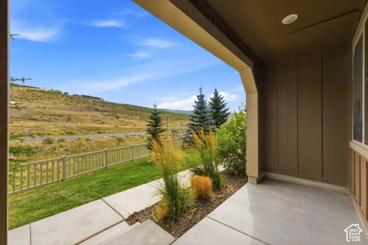 Covered concrete patio with recessed lighting, bordered by landscaped plantings, a concrete pathway, and a wooden fence