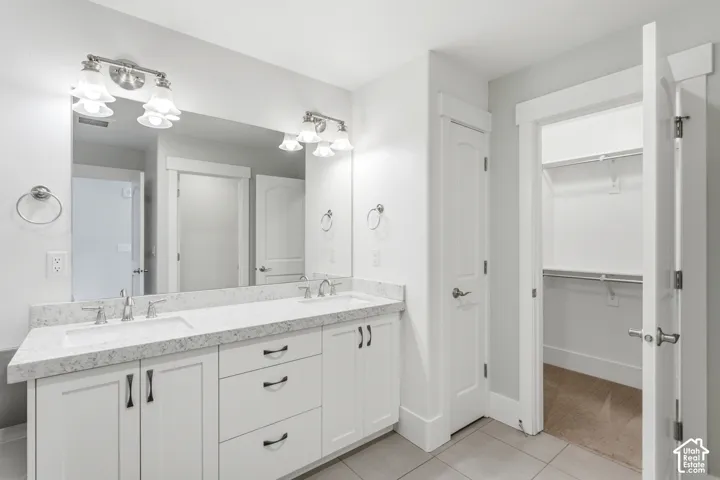 Dual vanity with undermount sinks, stone countertop, white cabinetry with dark hardware, and overhead lighting fixtures