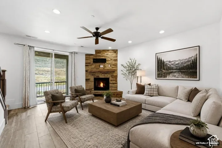 Stone-clad corner fireplace, wood-finish flooring, recessed lighting, ceiling fan, and sliding glass door