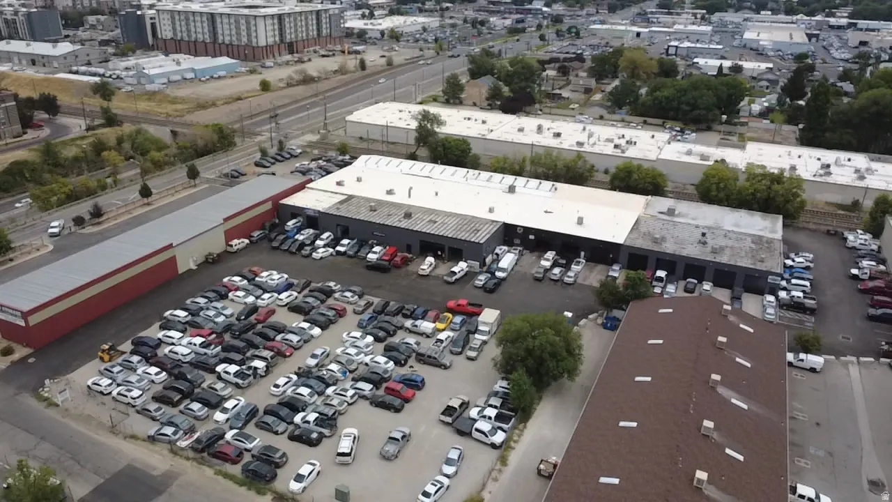 Multiple commercial buildings with varied rooflines, extensive paved and gravel parking areas, and a visible roadway