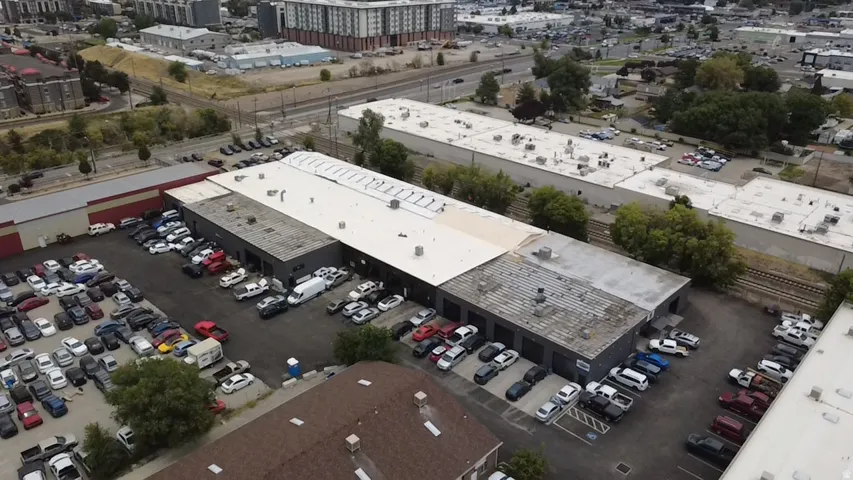 Expansive commercial property featuring multiple buildings with flat roofs, extensive paved parking areas, and adjacent railway lines