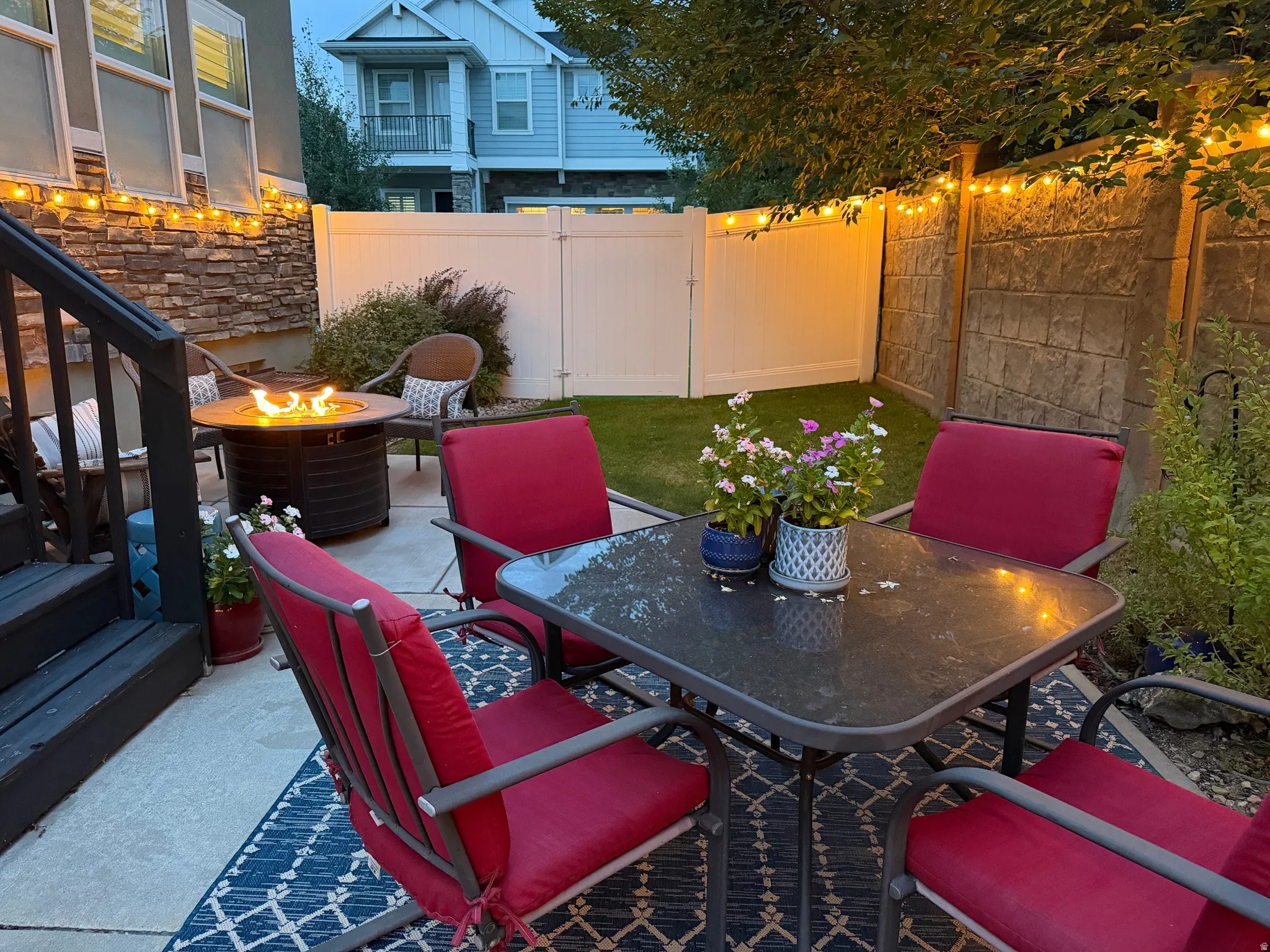 Paved patio area featuring a built-in fire pit, privacy fencing, and a manicured lawn