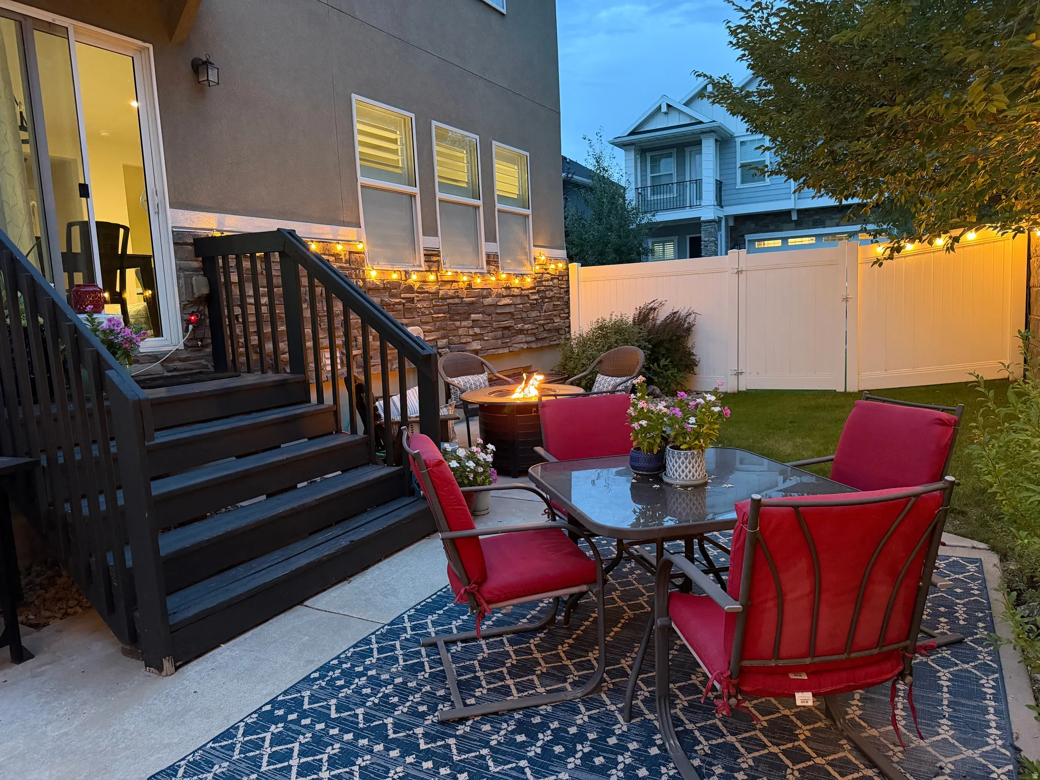 Rear patio with concrete slab, wood-finish stairs, stone veneer accent, and a white privacy fence