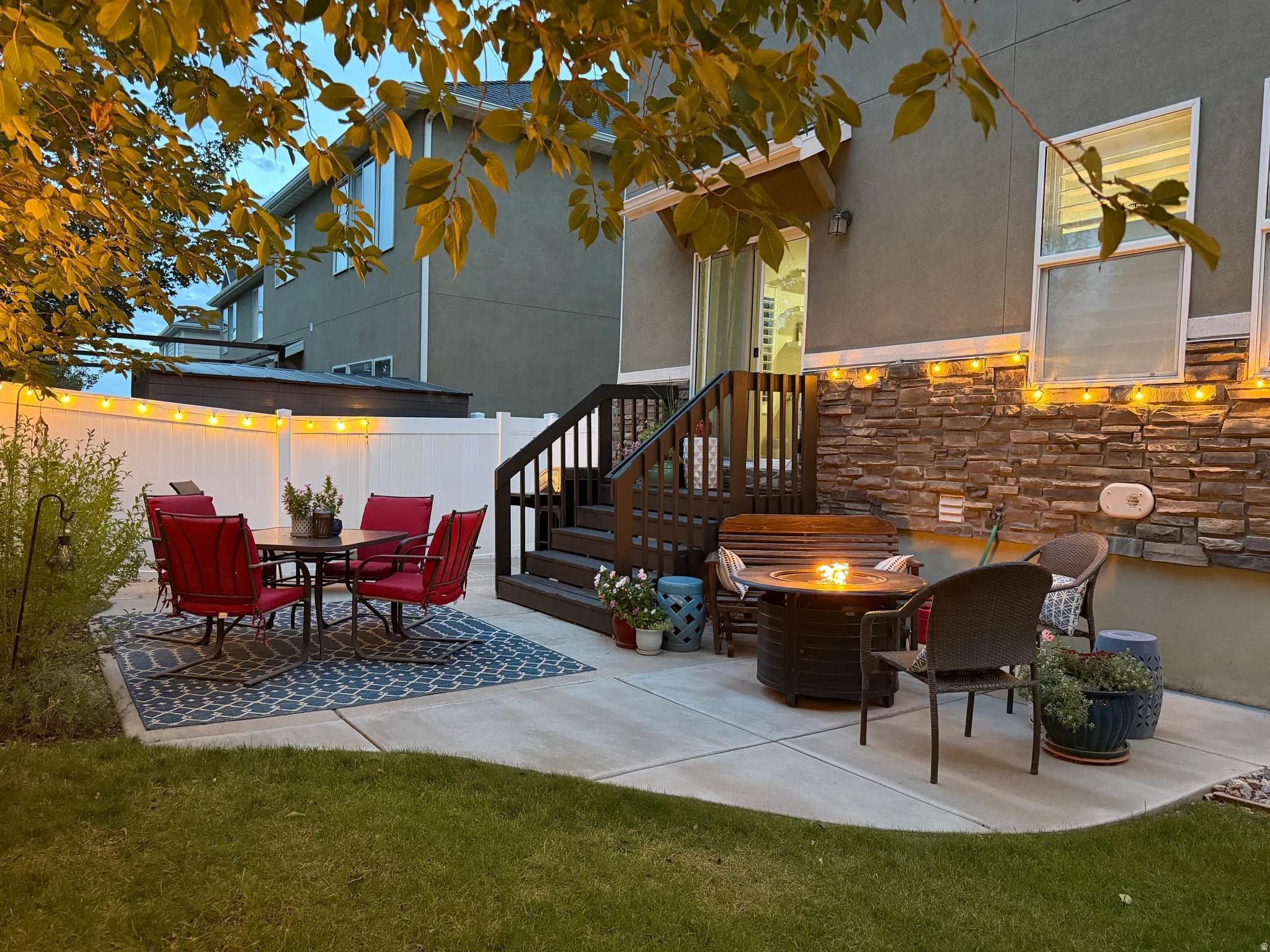 Concrete patio with a stone veneer accent wall, privacy fencing, and wood deck stairs