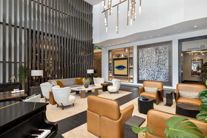 Spacious lounge area featuring a grand piano, a decorative wood slatted wall, recessed lighting, and a contemporary chandelier