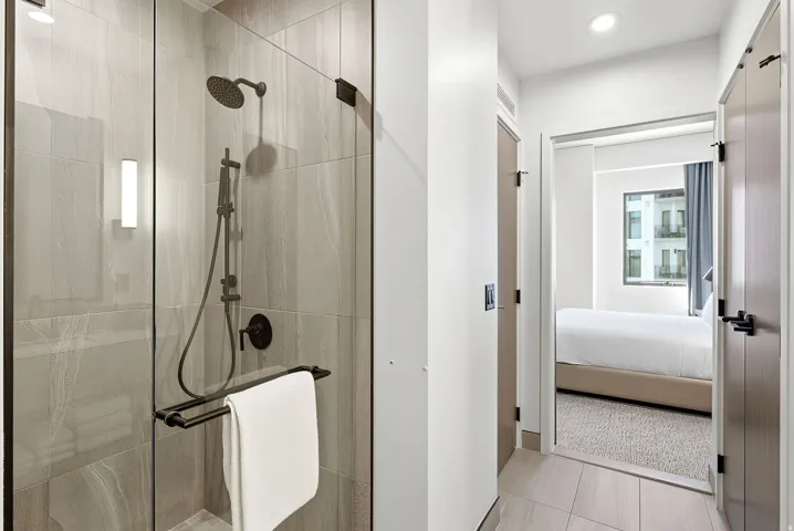 Glass-enclosed shower with a matte black rainfall showerhead and handheld sprayer