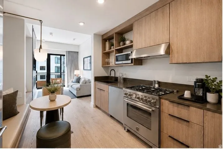 Contemporary kitchen featuring custom wood-finish cabinetry, stainless steel gas range with built-in oven, black countertops, and integrated shelving