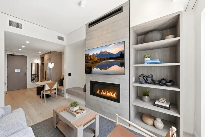 Integrated linear fireplace with concrete-finish surround, wood-finish flooring, built-in shelving, recessed lighting, and a dining nook with bench seating