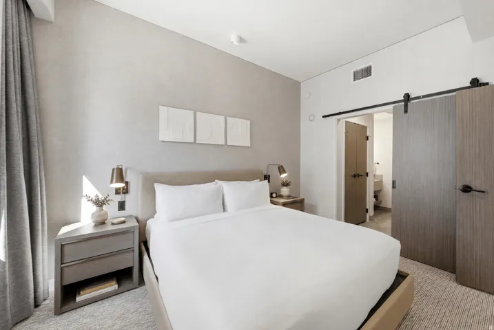 Barn door entry to an adjoining space, wood-finish flooring, bedside sconce lighting, textured wall finish, and built-in bedside table