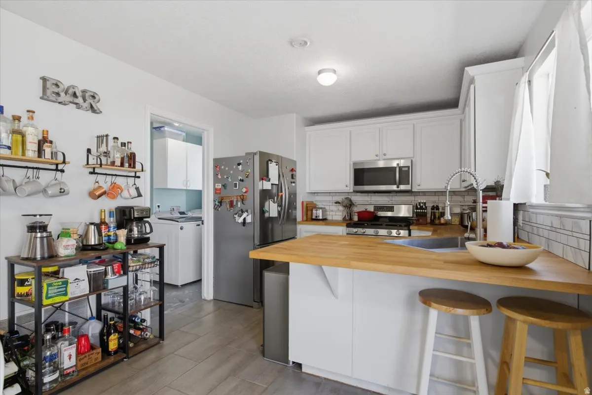 Kitchen featuring white cabinetry, stainless steel appliances, wood-finish countertops, and tile backsplash