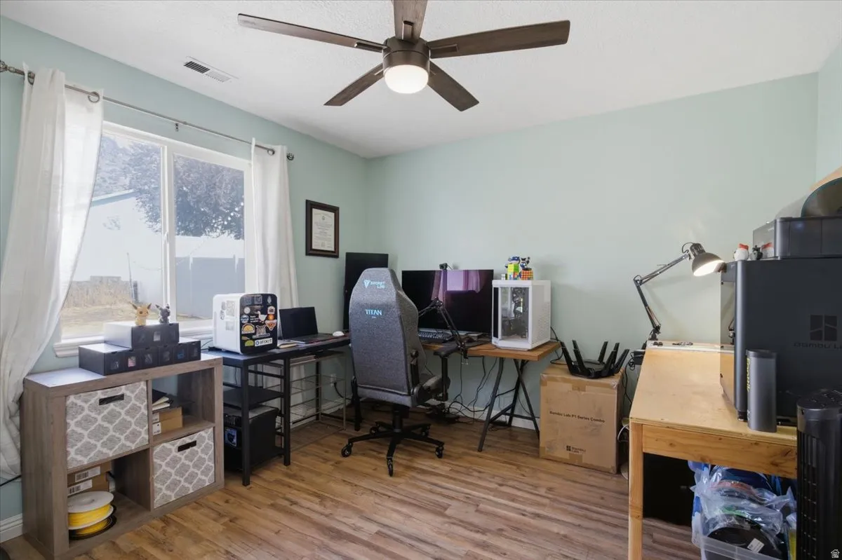 Wood-finish flooring, ceiling fan with integrated lighting, and a large window providing ample natural light