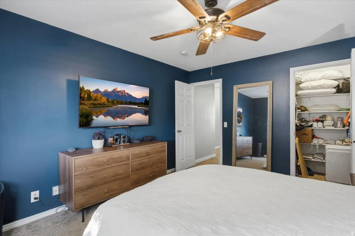 Ceiling fan with light fixture, carpeted flooring, and a closet with built-in shelving