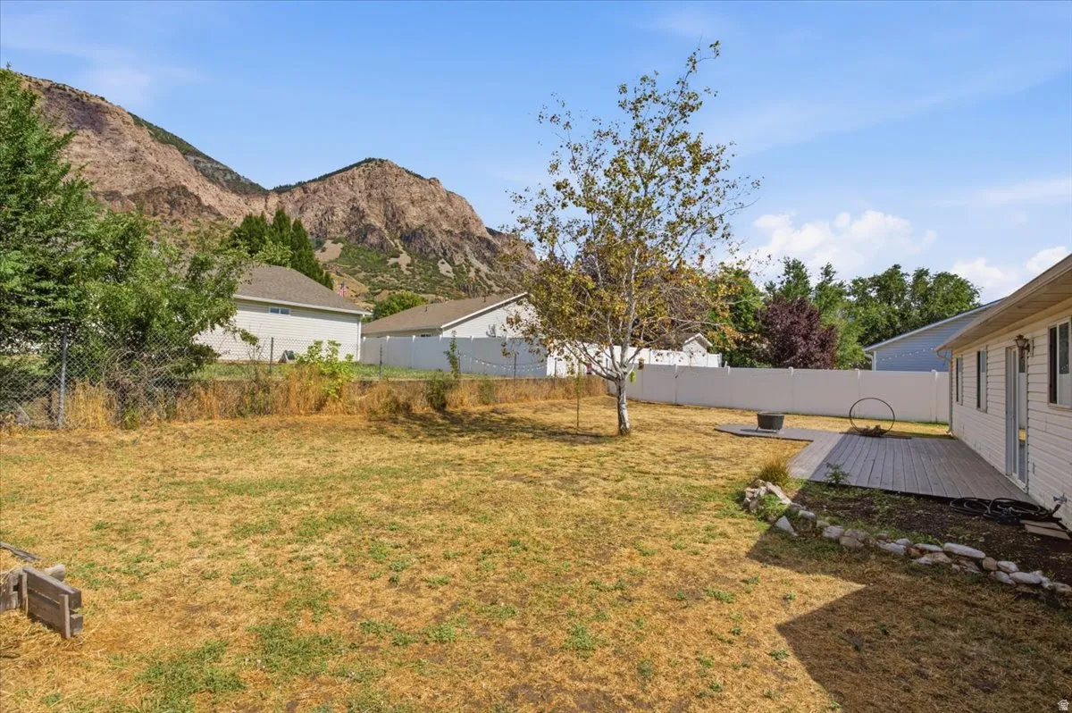 Expansive backyard featuring a natural rock backdrop, a privacy fence, and a spacious outdoor deck