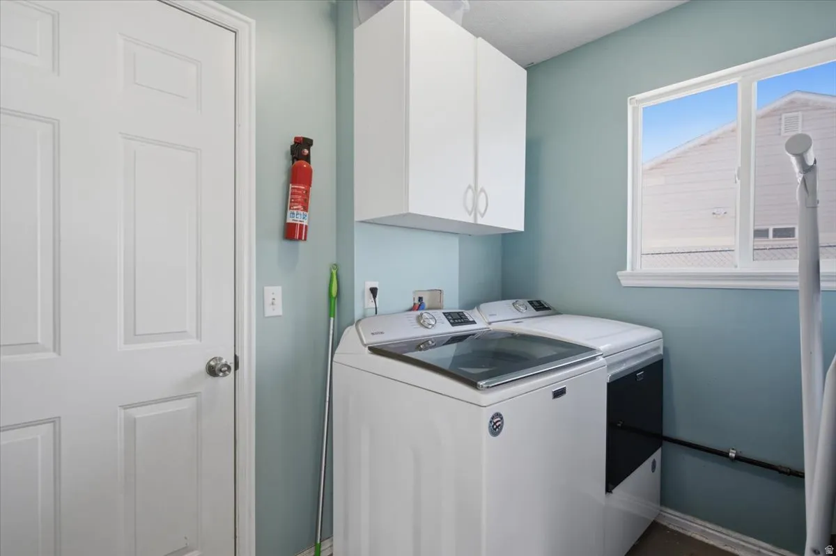 Utility room featuring a top-load washer and dryer, white cabinetry with ample storage, turquoise painted walls, a single-hung window with natural light, and a fire extinguisher for safety
