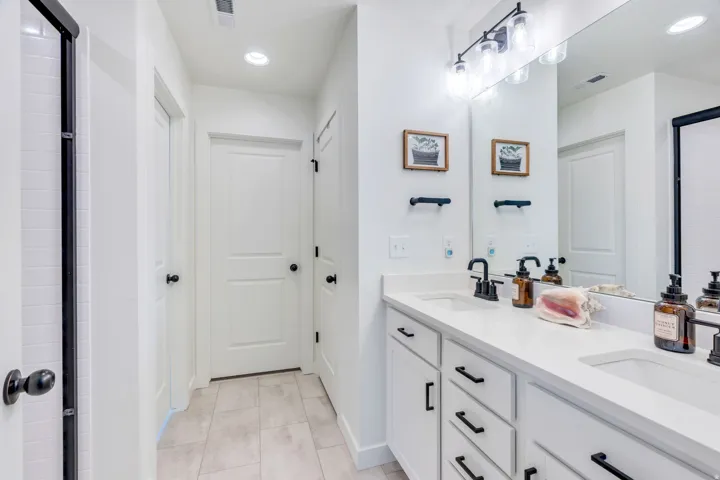 Dual-sink vanity with white cabinetry, quartz countertop, and matte black hardware anchors this bright bathroom