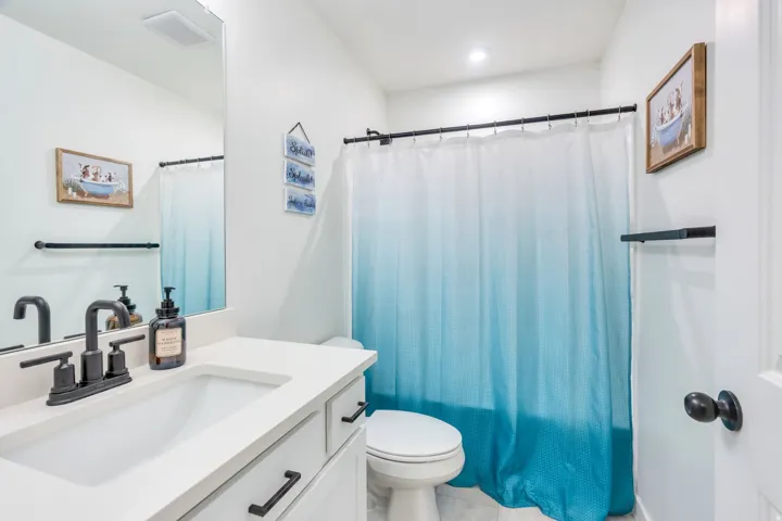 Contemporary bathroom featuring a white vanity with rectangular vessel sink, matte black hardware and faucet, quartz countertop, and ample mirror with integrated lighting