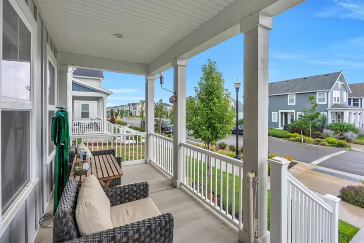 Covered front porch with concrete flooring, white balusters, and paneled siding