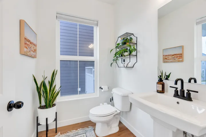 Pedestal sink with a matte black faucet, wall-mounted mirror, and wood-finish flooring