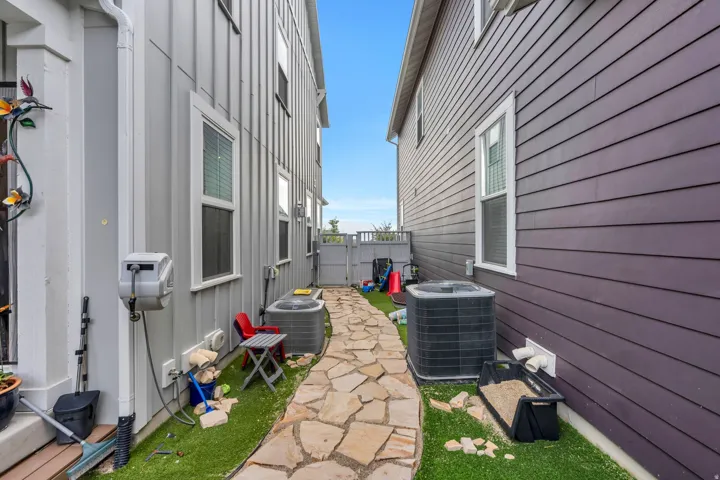 Charming side yard featuring a flagstone pathway, manicured lawn, and HVAC unit