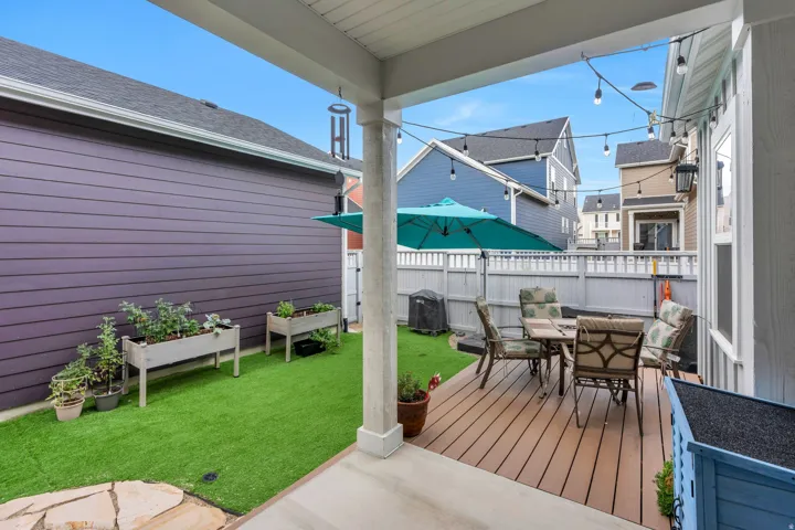 Expansive wood-finish deck, artificial turf yard, raised garden beds, and string lighting