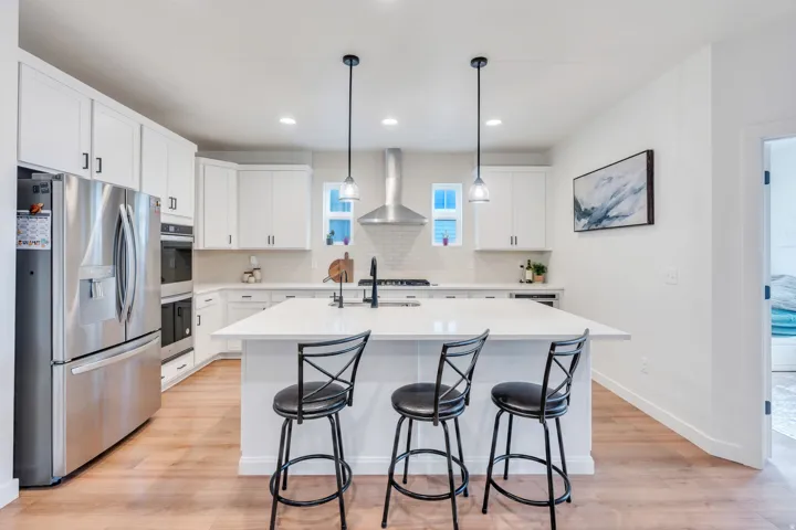 Kitchen featuring a large island with seating, stainless steel appliances, white cabinetry, and wood-finish flooring