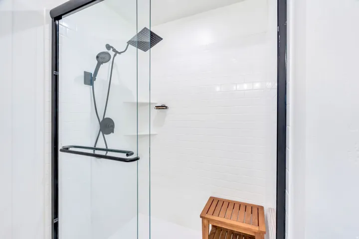 Frameless glass shower enclosure with matte black fixtures, white subway tile surround, recessed shelves, and a square rain shower head